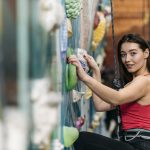 Una mujer sonriente escalando una montaña como metáfora del autocontrol y la superación personal para alcanzar una vida plena