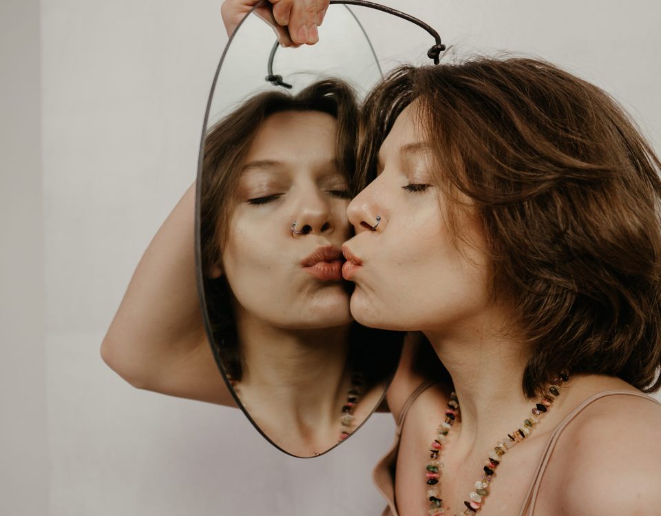 Una mujer se mira en el espejo y se da un beso, transmitiendo amor propio y confianza en sí misma. Una imagen que representa la importancia de la autoestima y el autodescubrimiento