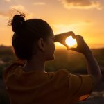 Imagen de una mujer haciendo el gesto de corazón con sus dos manos, bañada por el cálido rayo de sol, simbolizando la autoconfianza y la seguridad en uno mismo
