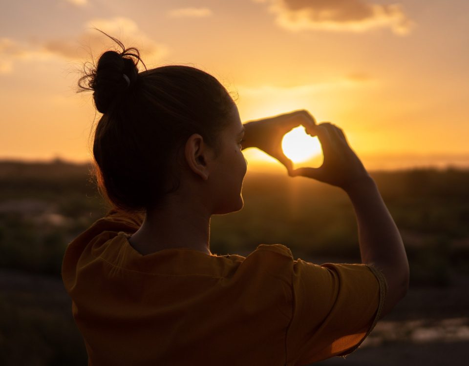 Imagen de una mujer haciendo el gesto de corazón con sus dos manos, bañada por el cálido rayo de sol, simbolizando la autoconfianza y la seguridad en uno mismo