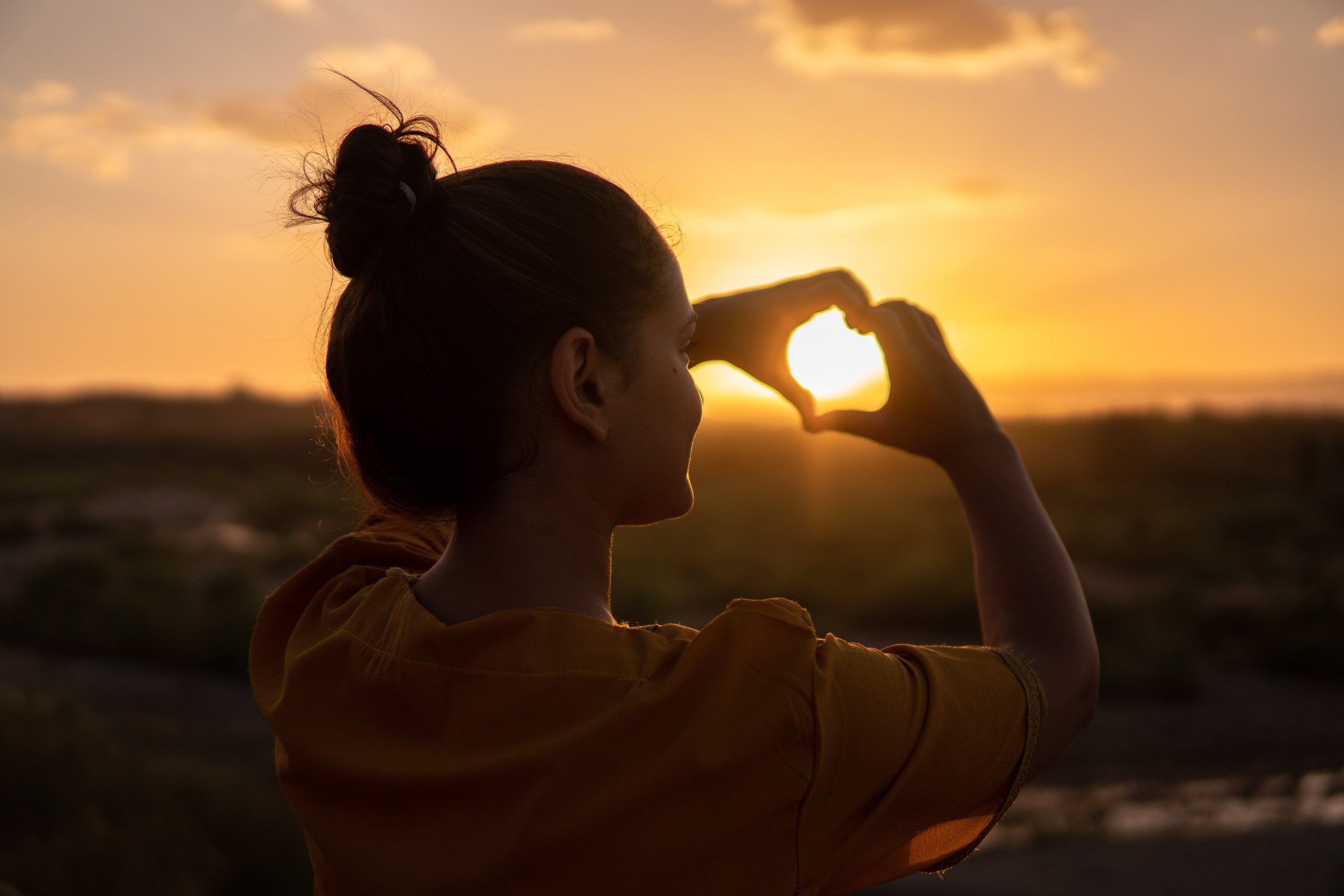 Imagen de una mujer haciendo el gesto de corazón con sus dos manos, bañada por el cálido rayo de sol, simbolizando la autoconfianza y la seguridad en uno mismo