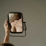 mujer viendo en el espejo y teniendo distorsión cognitiva de su imagen en la conducta alimentaria